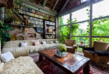 obývací pokoj ve zrekonstruované stodole s masívním dřevěným stolem, gaučem s kožušinami, retro křeslami, barevným tkaným kobercem, velikou knihovnou a prosklenou stěnou s výhledem na stromy