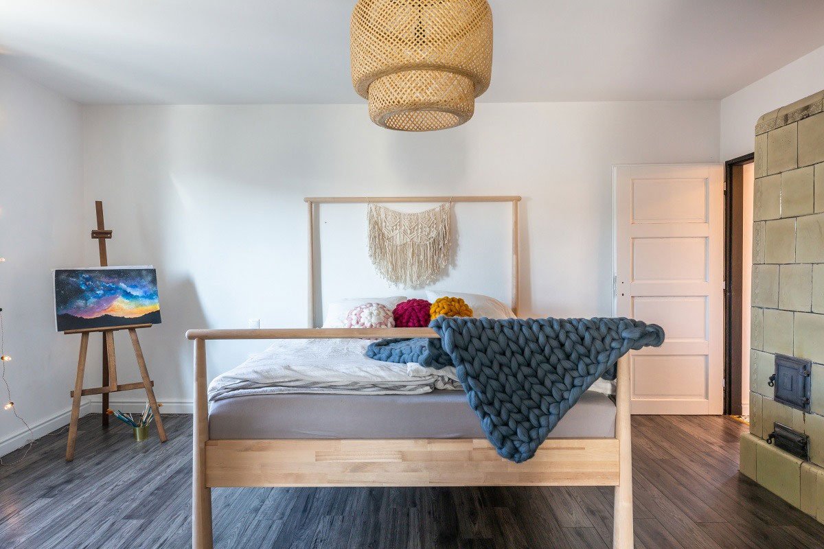 ložnice s dřevěnou postelí s vlněným pleteným přehozem