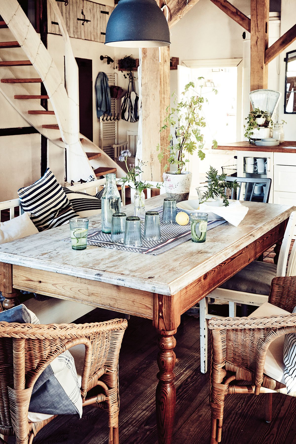 jídelna ve venkovském stylu, s dřevěným stolem, lavicí a proutěným křeslem, točitým schodištěm a dřevěnými trámy