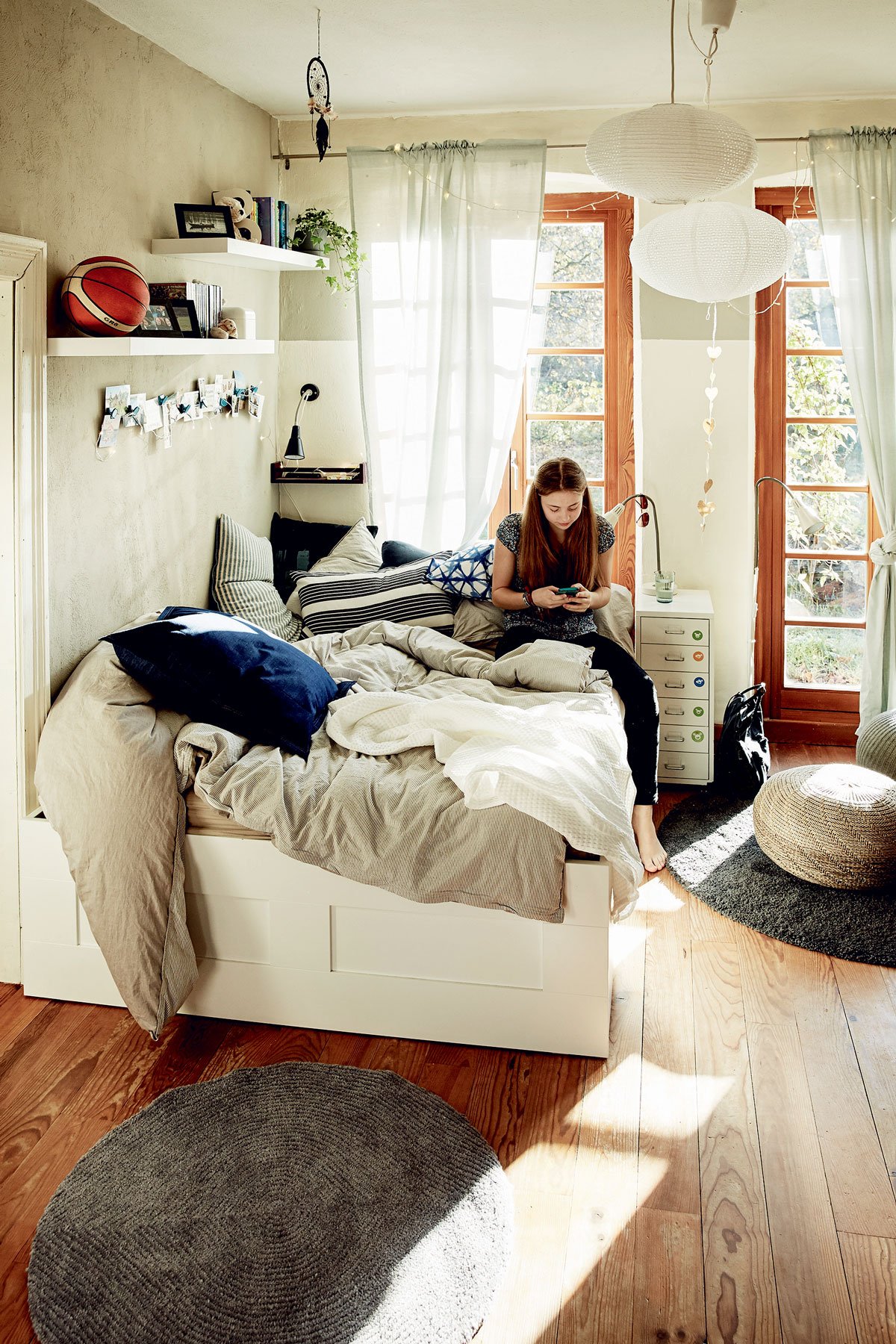 dětský pokoj s bílou postelí a povlečením v přírodních barvách, s policemi, nočním stolečkem a pleteným přírodným pufem
