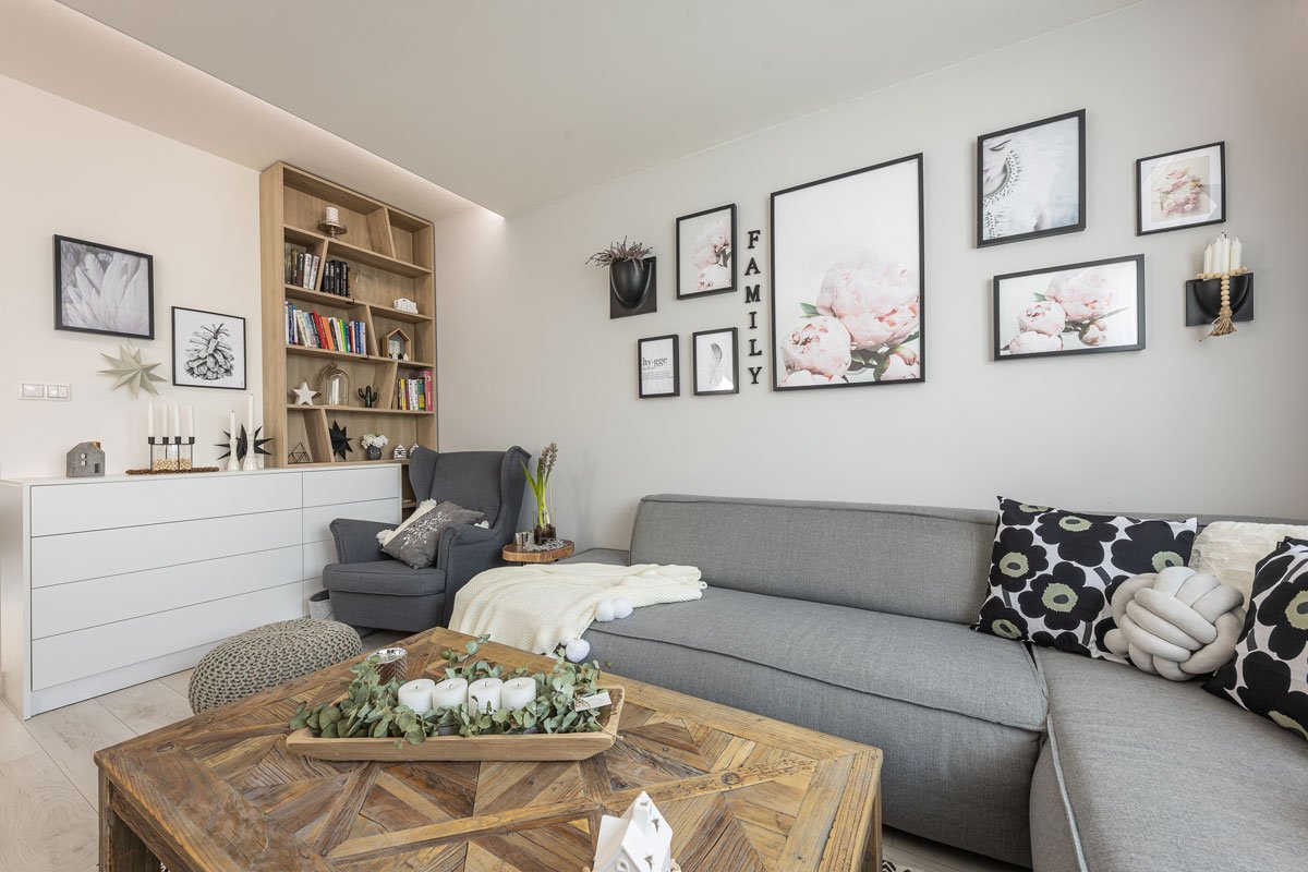 Obývací pokoj v severském stylu, s šedou pohovkou, dřevěným stolem a knihovnou a obrazy