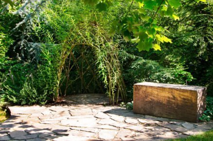 zahrada s altánkem z vrbového proutí a dřevěným hranolem na posezení
