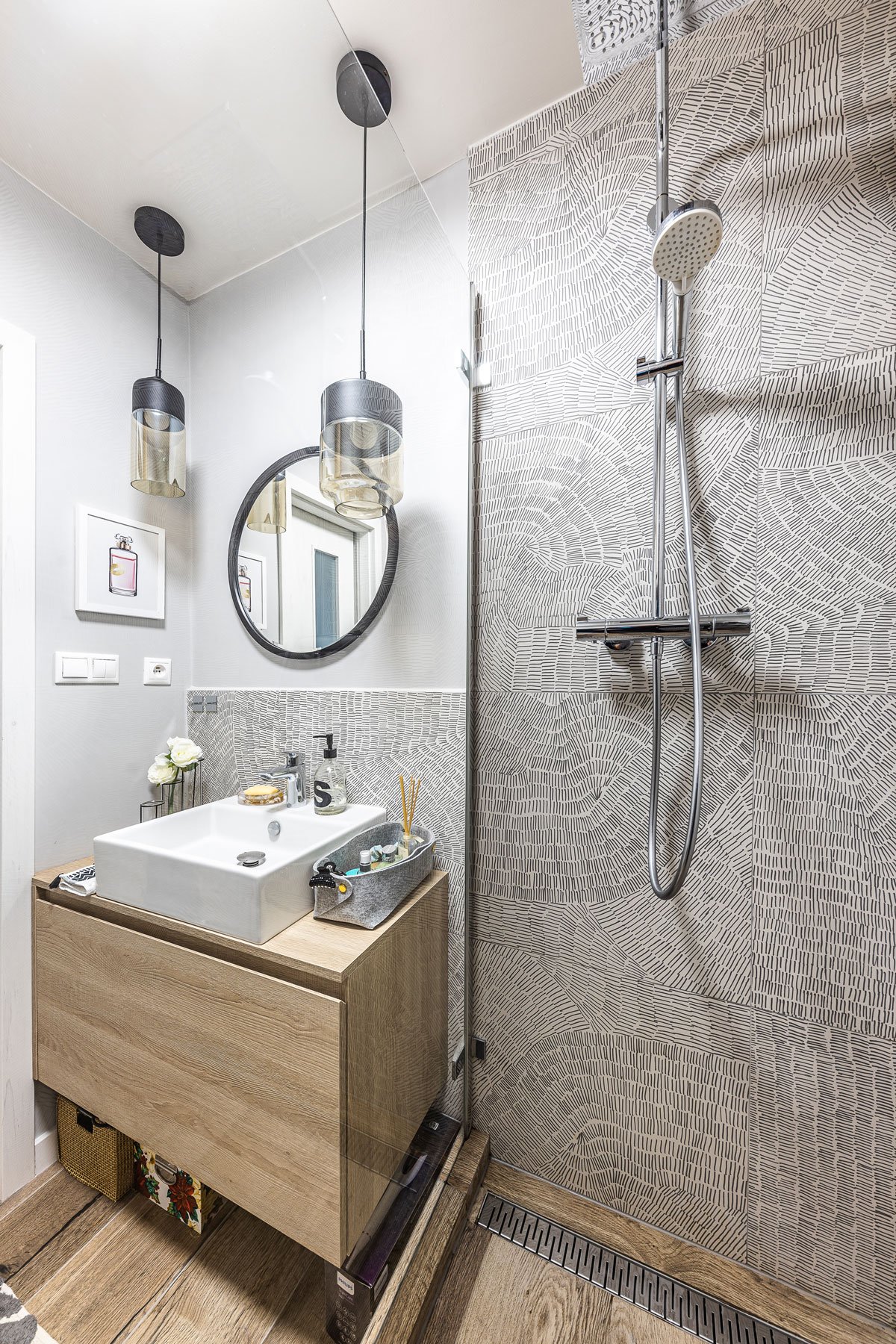 koupelna se vzorovaným obkladem, dřevěnou skříňkou s umyvadlem, sprchovým koutem, zrcadlem a závěsnými svítidlami