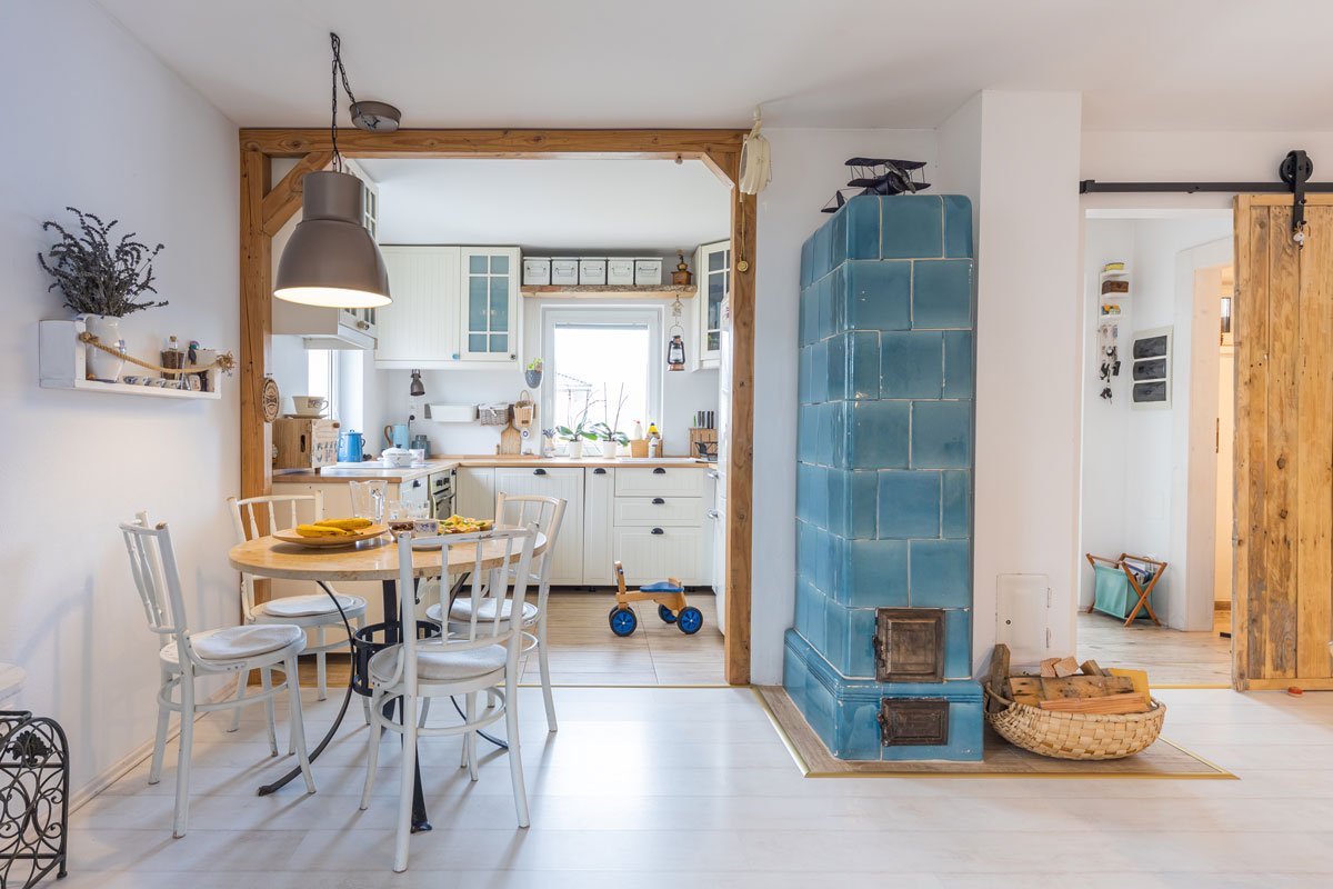interiér s bílou kuchyní, jídelním stolem, ručně vyrobenou policí, dřevěnými trámy, stoletými modrými kamny a posuvním systémem barn doors