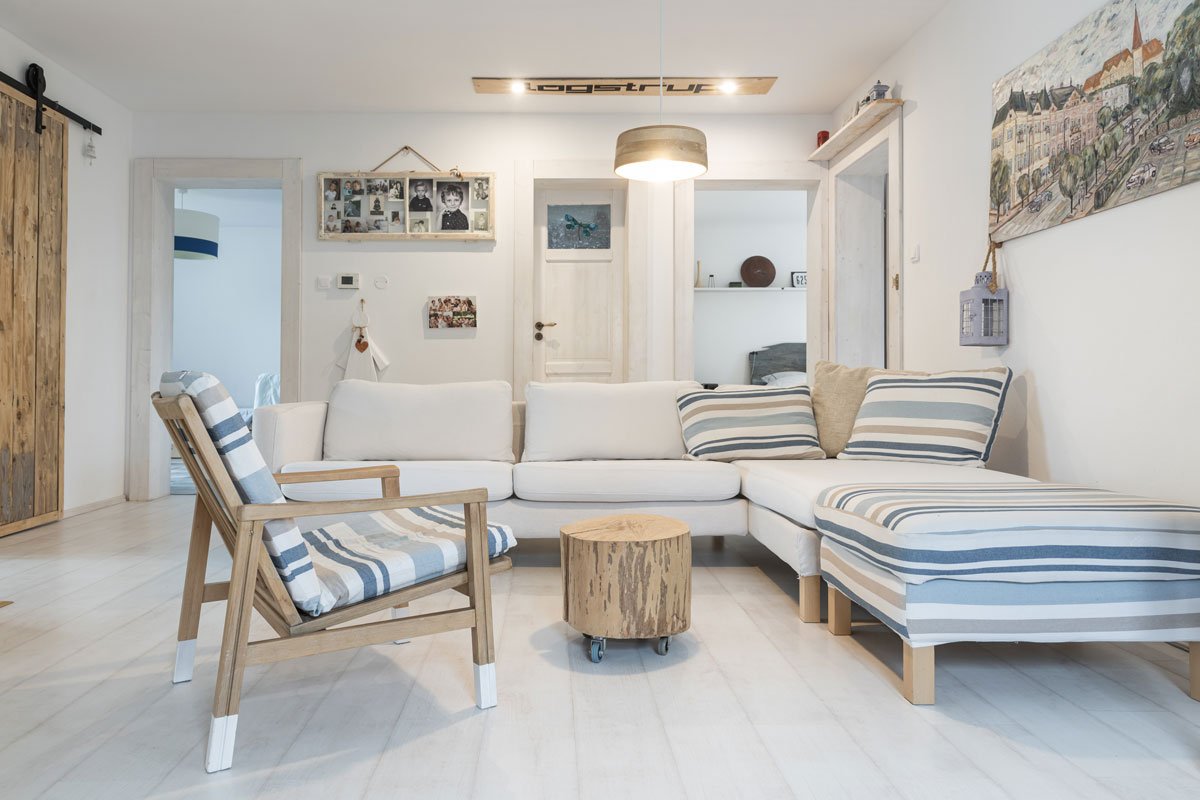 obývací pokoj s bílou sedací soupravou, zrenovovaným křeslem a stolkem z kulatiny