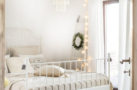 Romantická ložnice v bílé barvě, s kovovou postelí a pleteným kobercem.
