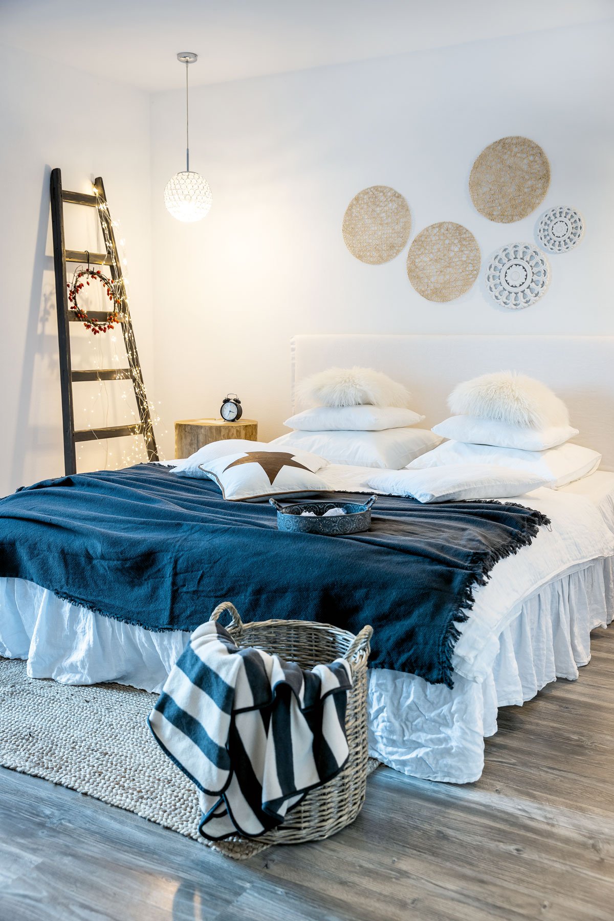 ložnice ve venkovském a skandinavském stylu s žebříkem se světelnou řetezí a dekoracemi na stěně nad postelí vyrobenými z prostírání