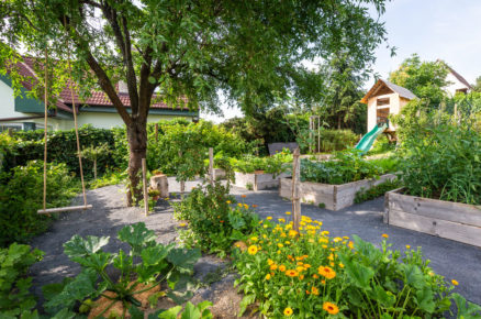 zahrada vybudovaná ve svahu, bez trávníku, s vyvýšenými záhony se zeleninou a bylinkami, domkem pro děti a houpačkou na stromě