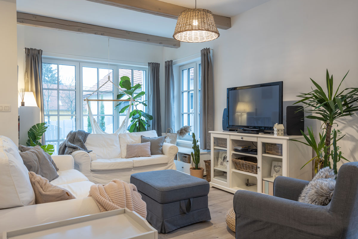Obývací pokoj ve venkovském stylu s bílou pohovkou a sivým křeslem a taburetem