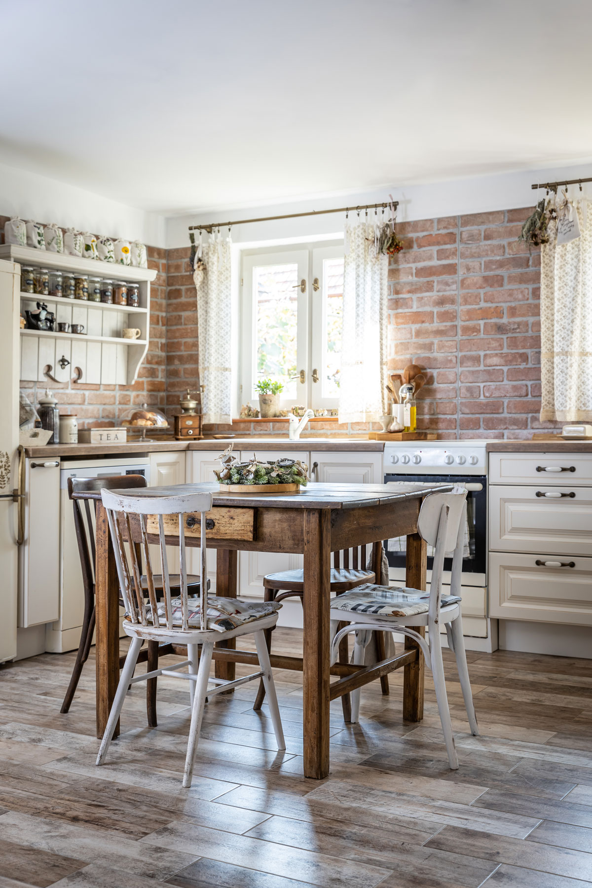 venkovská kuchyň so světlou kuchyňskou linkou, cihlovým obkladem na stěně a podlahou s imitací dřeva