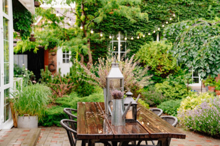 Zahrada s terasou , okrasnými záhony a stromy a dřevěným stolem se židlemi