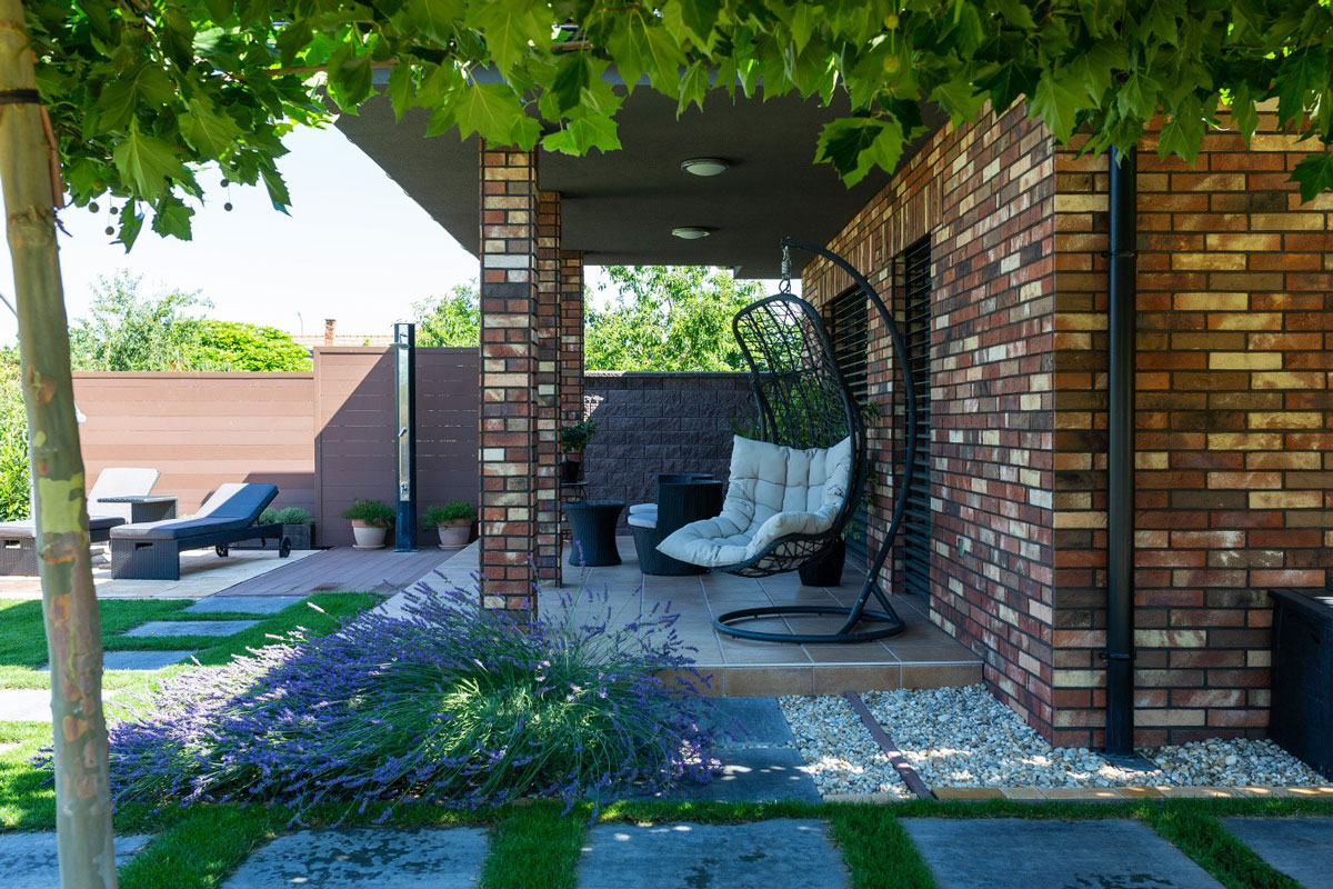 rodinný dům s cihlovým obkladem, terasou se zahradním nábytkem, houpačkou, solární sprchou a lehátkami