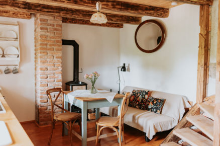 Venkovský interiér chalupy s pohovkou, dřevěným stolem, židlemi, na stropě jsou přiznané trámy
