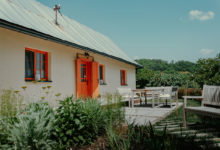 chalupa s oranžovými okny a dveřmi, v přední části je terasa se zahradním sezením