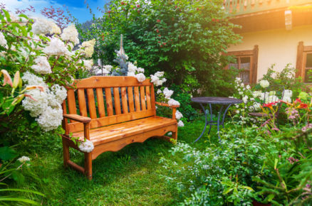 Zahrada s lavičkou, kovovým stolkem a židlí a okrasnými záhony