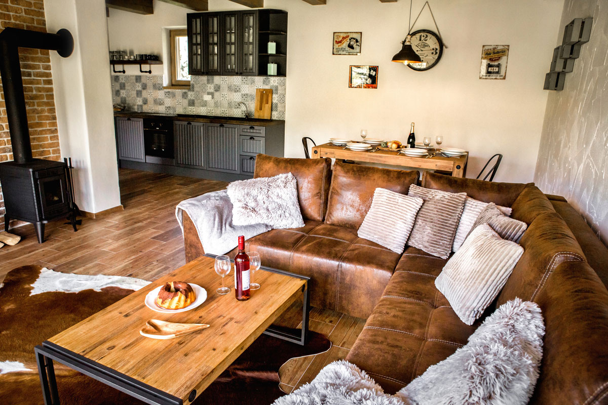 obývací pokoj, jídelna a kuchyň v industriálním stylu, kožená sedačka, masivní stolky a sivá kuchyň