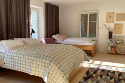 ložnice v moderním venkovském stylu s dřevěnými postelemi, světlou podlahou a barevným geometrickým kobercem