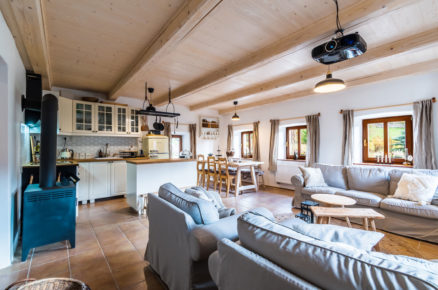 obývák a kuchyň ve venkovském stylu s krbovými kamny, bílou kuchyní a dřevěnými stropy
