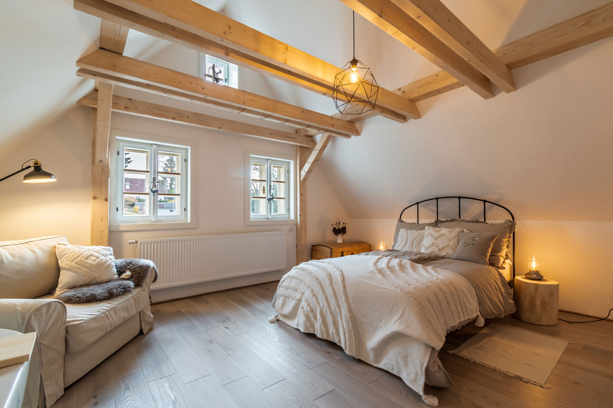 ložnice ve venkovském přírodním stylu s kovovou postelí a stropními trámy
