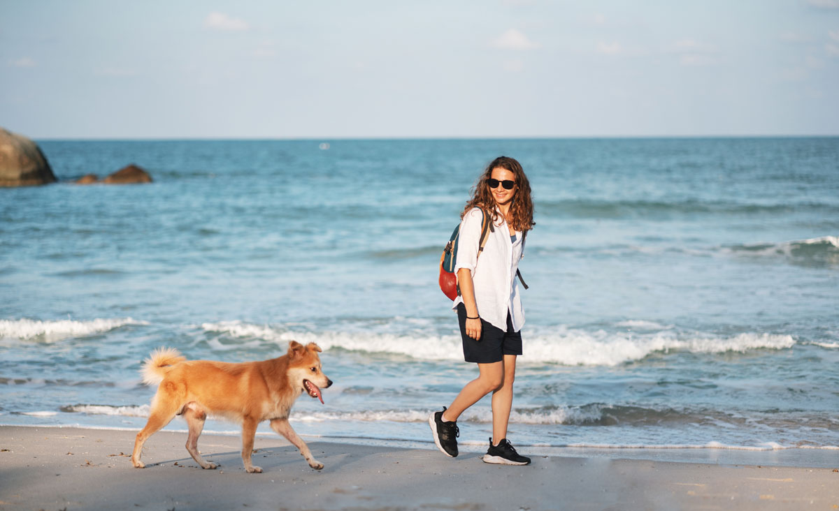 Žena se prochází po pláži se psem
