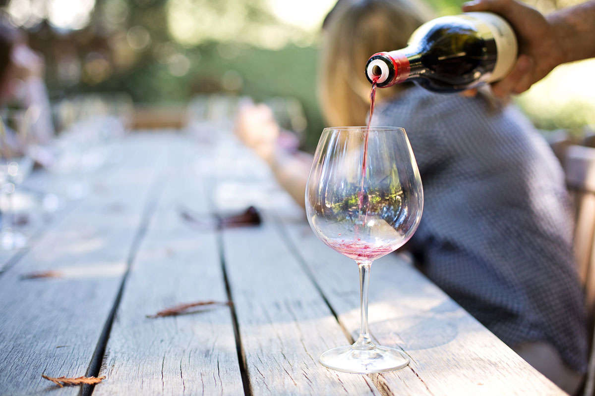Sklenička stojící na dřevěném stole, do které se leje víno.