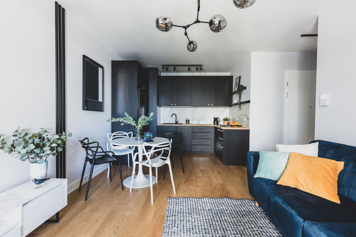malý byt s otevřeným prostorem s černou kuchyní, jídelním bílým stolem a obývacím pokojem s modrou sedačkou