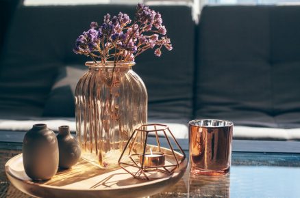 skleněný stůl s dřevěným podnosem, na kterém je skleněná váza, kovový a metalický svícen