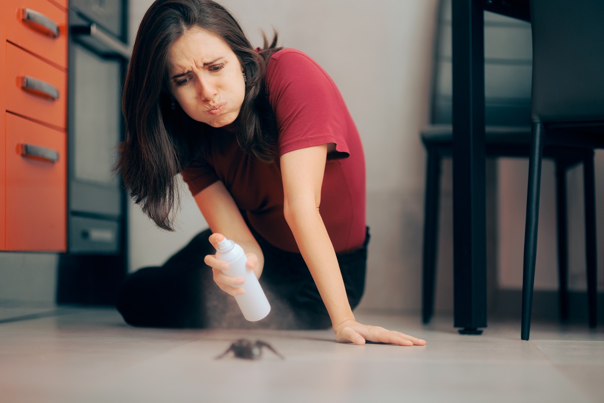 Žena striekajúca insekticídom na mravca v kuchyni