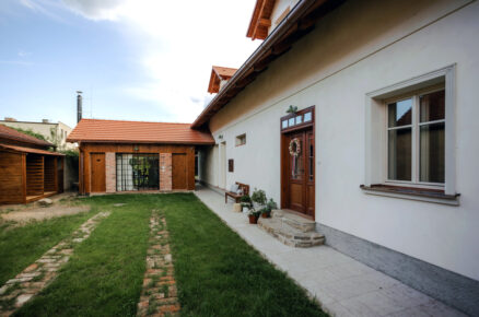 Upravený venkovní dvorek s travnatou plochou, cihlovými stopami a výhledem na zadní část chalupy.