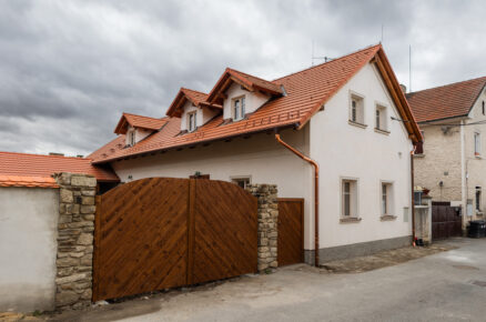 Tradiční zrekonstruovaný venkovský dům s červenou střechou, dřevěnými vraty a kamenno-cihlovým oplocením.