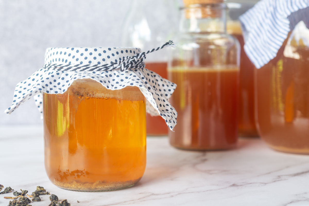 lahev na komuchu kombucha ve skleněné nádobě s papírovou utírkou jako vrhcnák