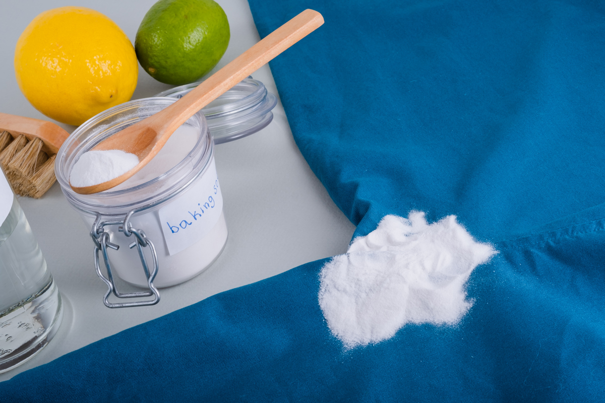 soda Jedlá soda vysypaná na modrý textil, v pozadí citron, limetka, dřevěný kartáč a sklenice s nápisem „baking soda“.
