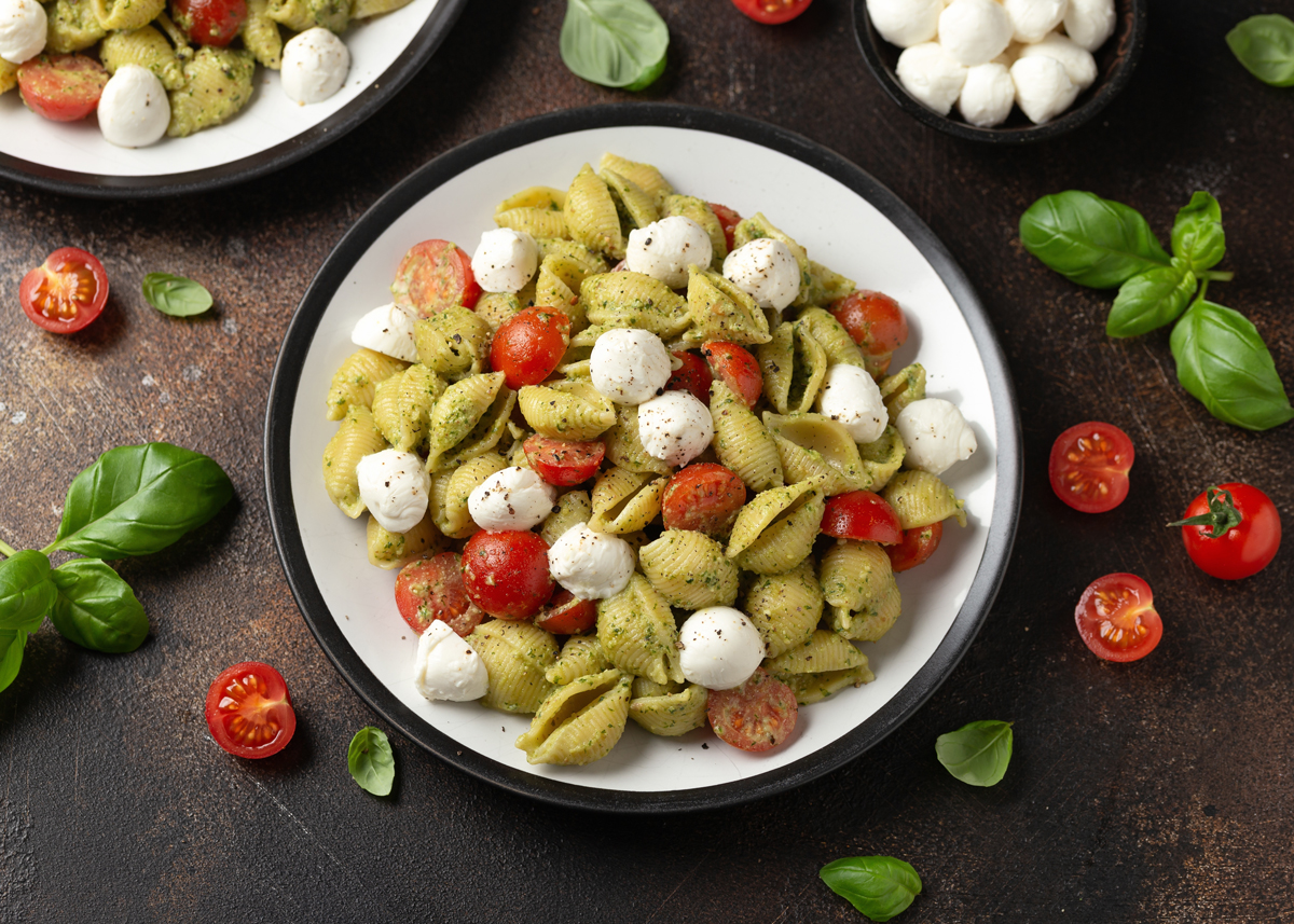testoviny a pesto Talíř těstovin ve tvaru mušliček s pestem, cherry rajčaty a kuličkami mozzarelly, ozdobený čerstvou bazalkou.