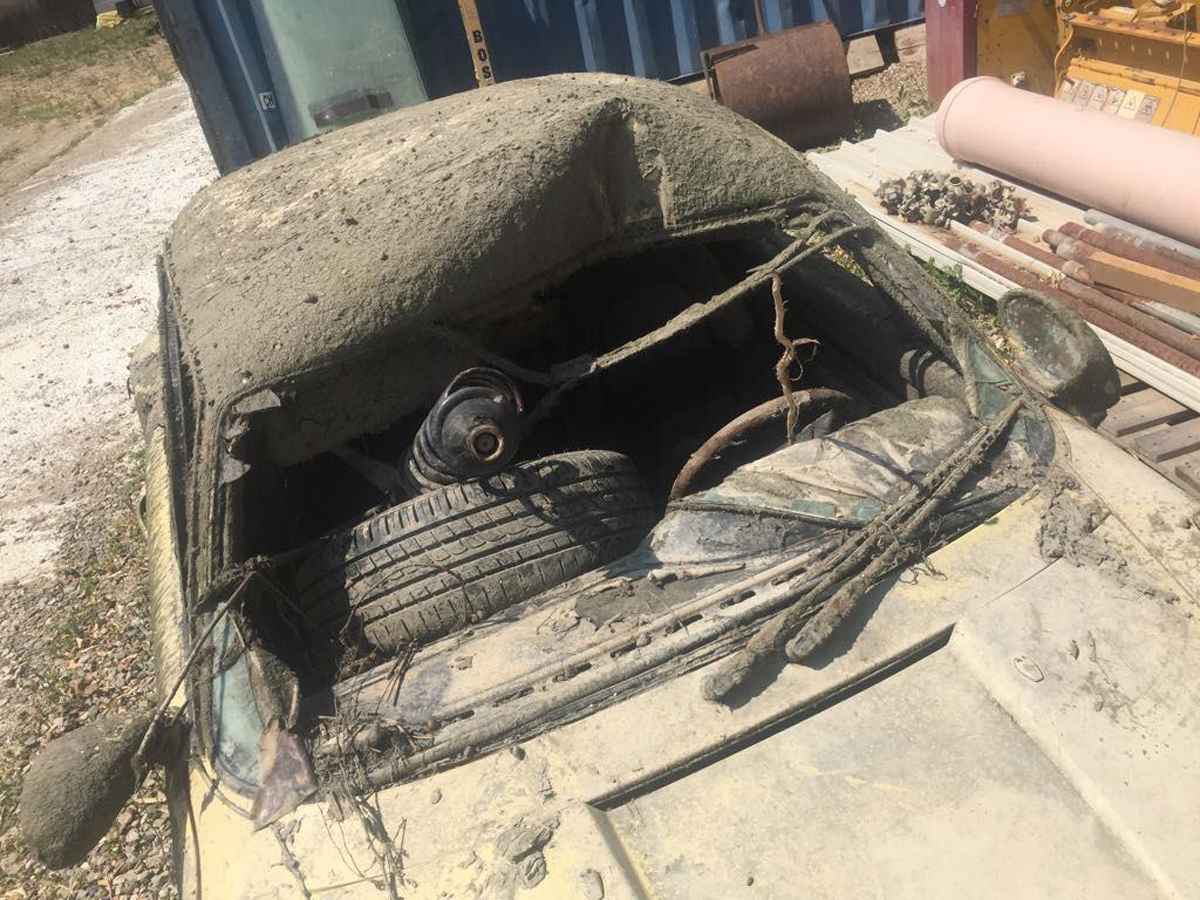 Detailní pohled na poničenou střechu a přední část Porsche 911 s pneumatikou a větvemi uvnitř, důsledek dlouhodobého ponoření.