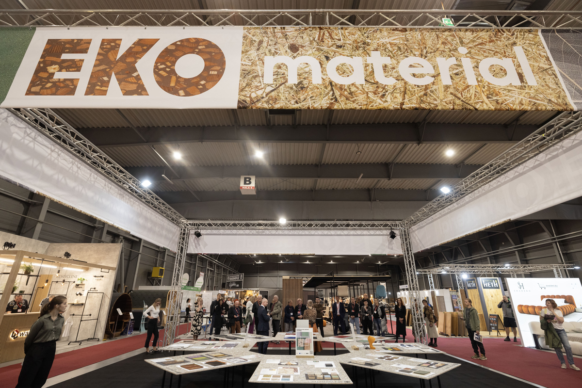 Expozice „EKO materiál“ na veletrhu – velký banner v hale, stoly se vzorky a skupiny návštěvníků v zóně.