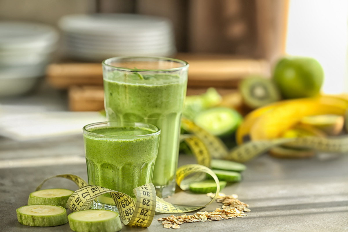 Zelené smoothie z cukety, banánu a kiwi ve sklenicích, kolem pásmo a suroviny – zdravé hubnoucí pití.