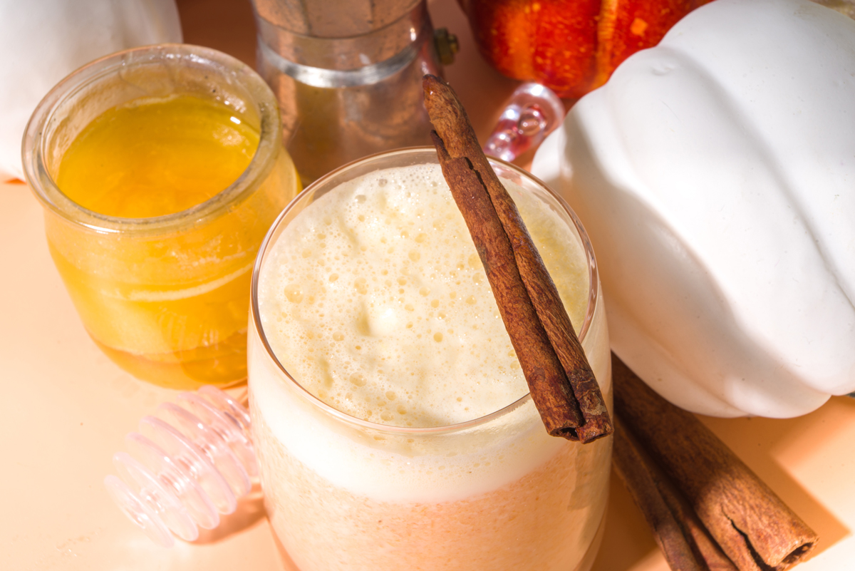 Sklenice smoothie ozdobená skořicí, vedle med a dýně.