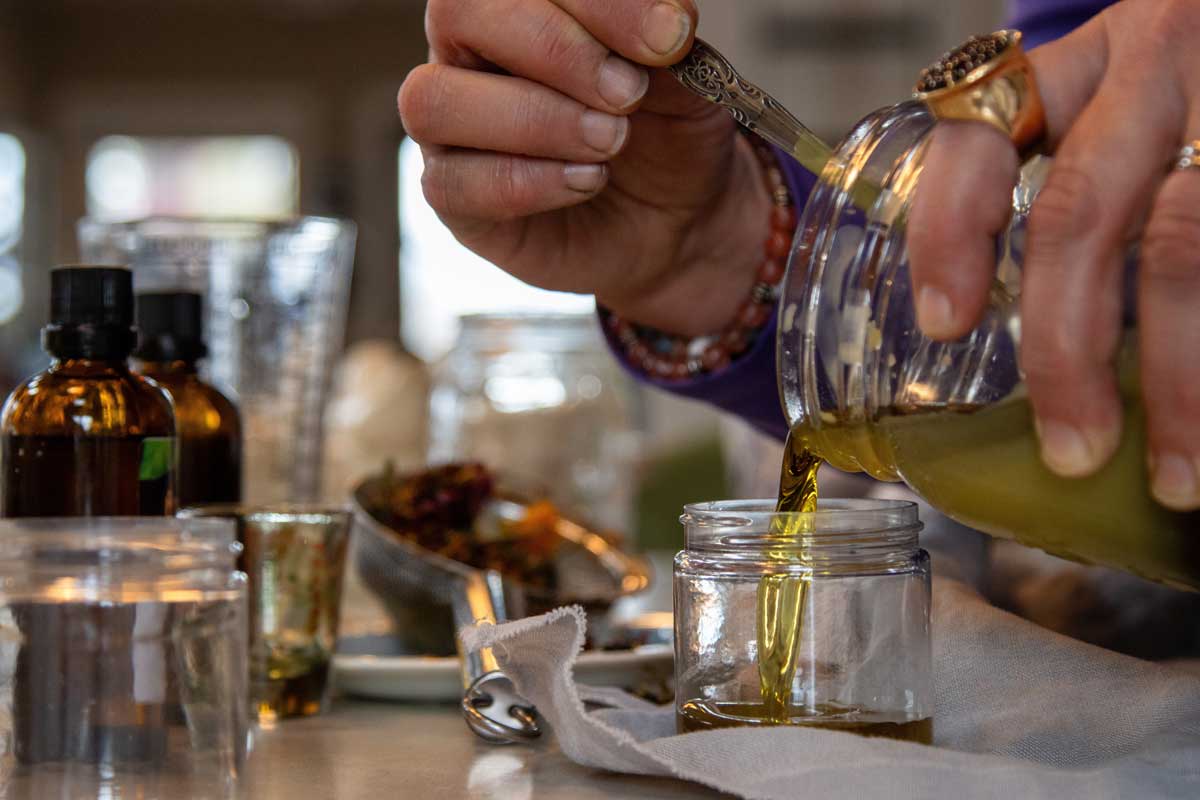 Nalévání tekuté bylinné směsi do kovových dóz při výrobě balzámu na ucpaný nos.