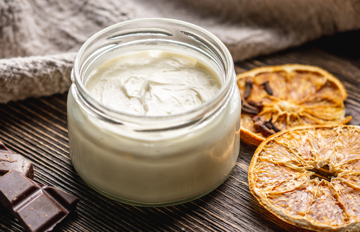 domaci citrusove telove maslo Sklenička s domácím citrusovým tělovým máslem obklopená sušenými plátky pomeranče a kousky čokolády.