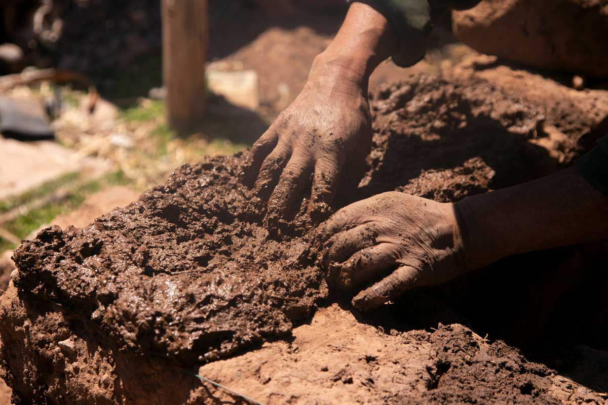 hlinena omitka Ruce člověka tvarující hliněnou směs při stavbě tradiční stěny.