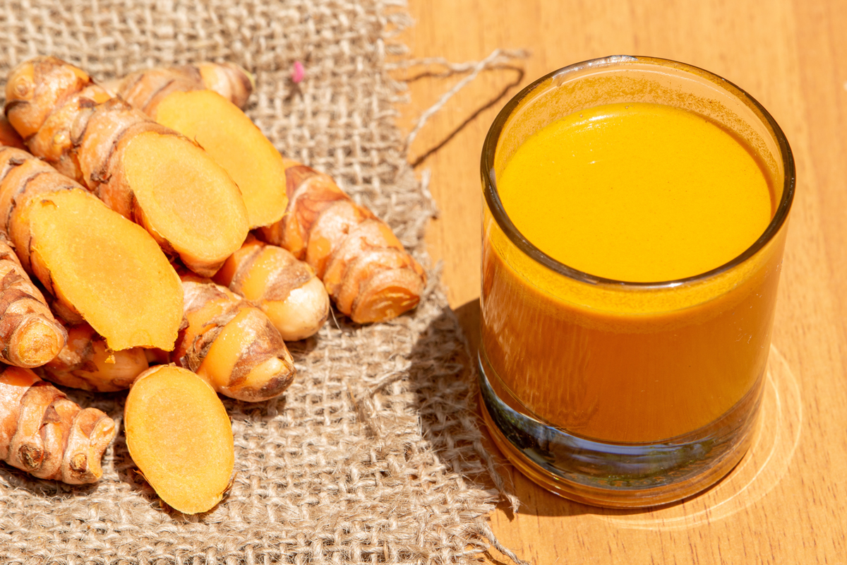 kurkumovy sot Sklenice s kurkumovým shotem a plátky čerstvé kurkumy na jutovém podkladu.