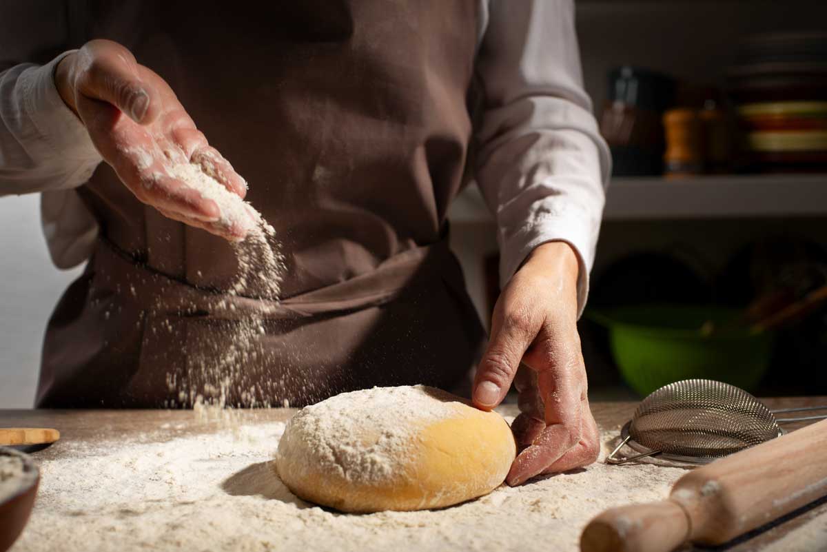 mouka Ruce posypávající mouku na bochánek těsta při domácím pečení.