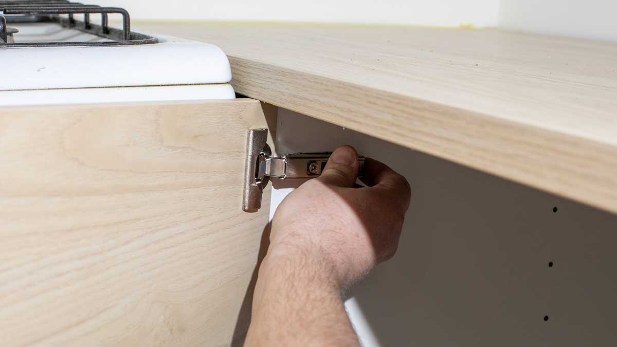 Montáž nového kuchyňského pantu na dvířka skříňky během opravy kuchyňské linky.