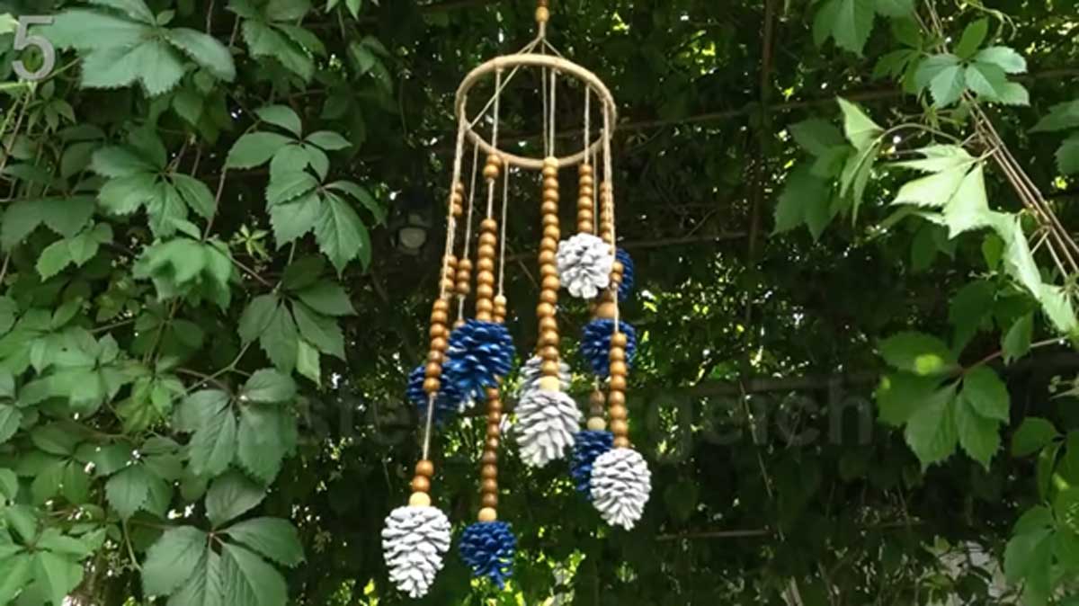 Barevně natřené šišky a dřevěné korálky zavěšené jako venkovní ozdoba.