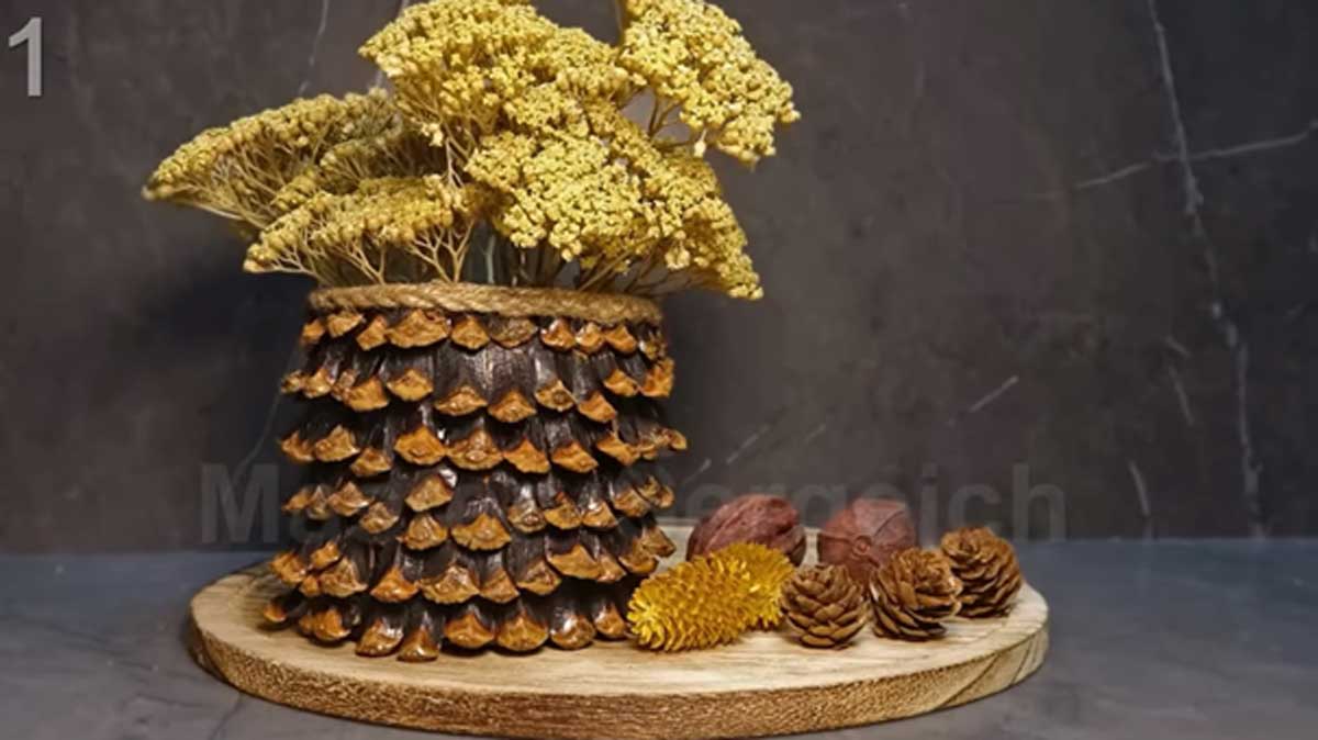 Ručně vyrobená váza ze šiškových šupin se žlutými sušenými květinami.