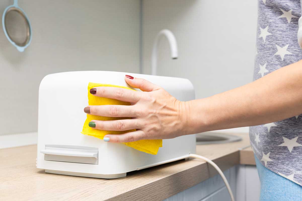 Žena bezpečně čistí vnější plášť topinkovače jemným hadříkem bez rizika poškození elektrických částí