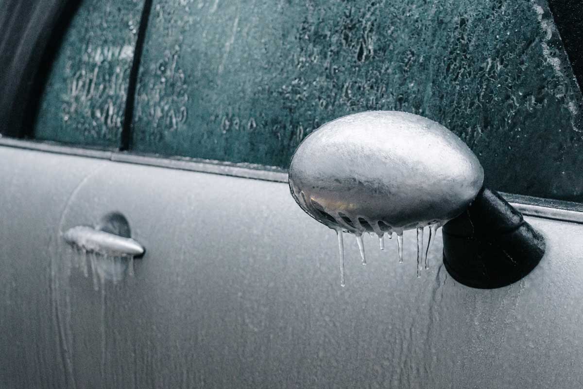 Zamrzlá klika a zpětné zrcátko osobního auta pokryté ledem během zimního rána.