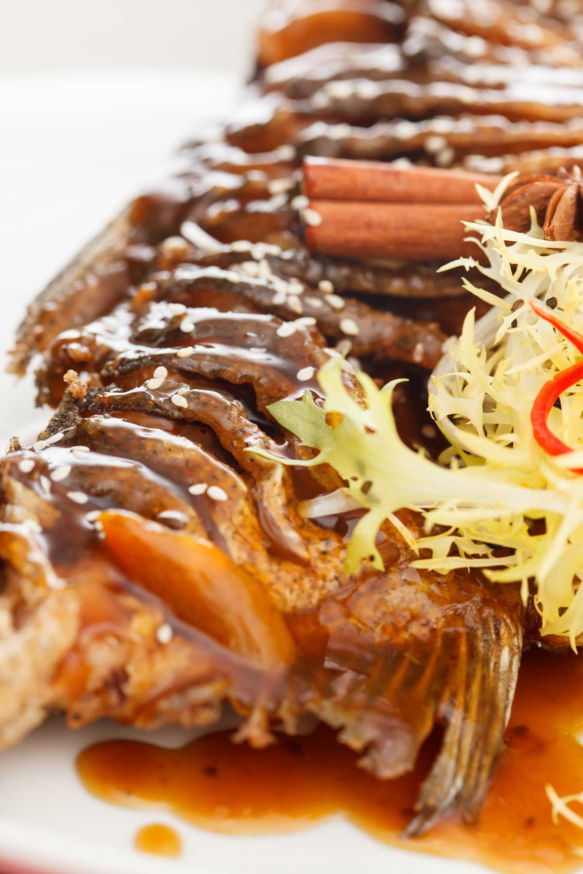 Detail kapra na černo přelitého hutnou lesklou omáčkou s kořením a sezamem připraveného podle starých svátečních receptů