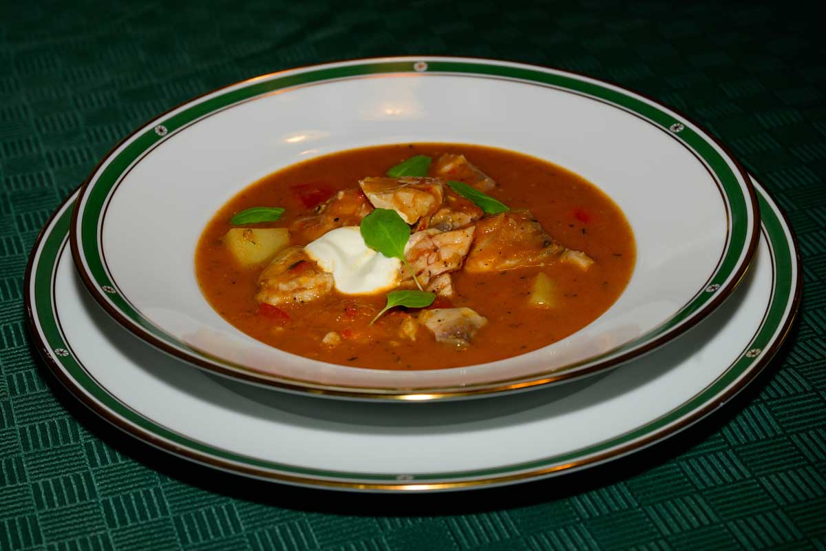 Porce tradičního kapřího guláše s brambory a paprikou ozdobená smetanou a zelenými lístky servírovaná v porcelánovém talíři