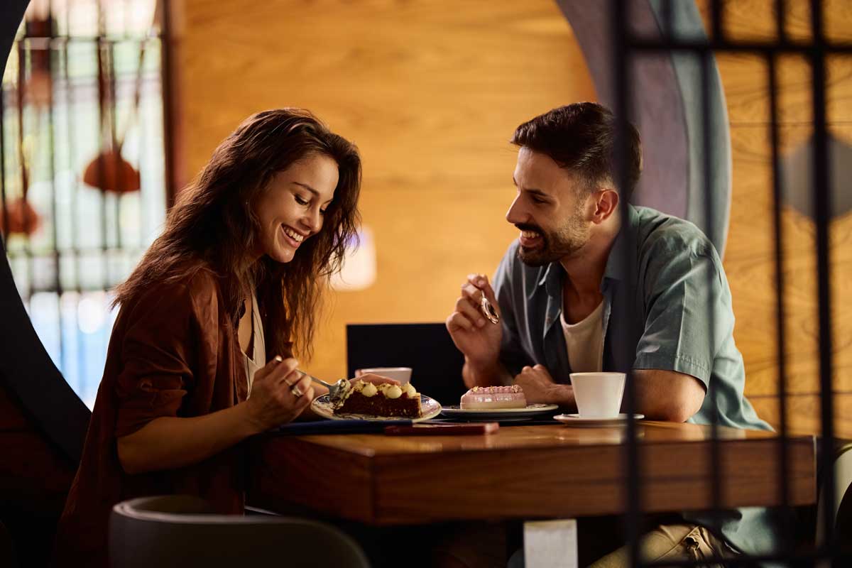 Mladý pár sedící v kavárně u stolu s dezertem a kávou, usmívají se na sebe